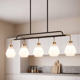Five-light kitchen island pendant with frosted white glass shades, black metal frame, and brass accents, hanging over a kitchen counter