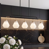 Five-light kitchen island pendant with frosted white glass shades, black metal frame, and brass accents, hanging over a dark marble countertop