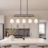 Five-light kitchen island pendant with frosted white glass shades, black metal frame, and brass accents, hanging over a white countertop in a modern kitchen