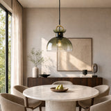 Brass pendant light with gradient green glass dome shade hanging over a round marble dining table