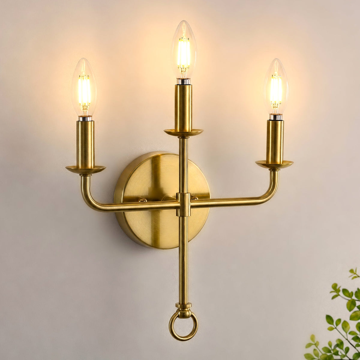 Three-light gold brass wall sconce with candle-style bulbs, shown mounted on wall