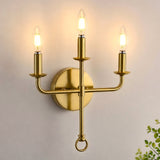 Three-light gold brass wall sconce with candle-style bulbs, shown mounted on wall