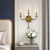 Three-light gold wall sconce with brass finish, mounted on bedroom wall above nightstand