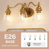 Gold bathroom vanity light with three clear glass bell shades, shown mounted on tiled wall above mirror