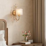Gold crystal leaf wall sconce with fabric shade mounted on beige wall beside bed
