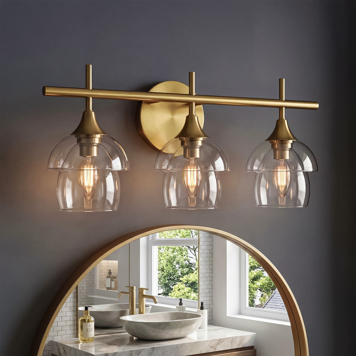 Gold bathroom vanity light with three clear glass shades mounted above a mirror