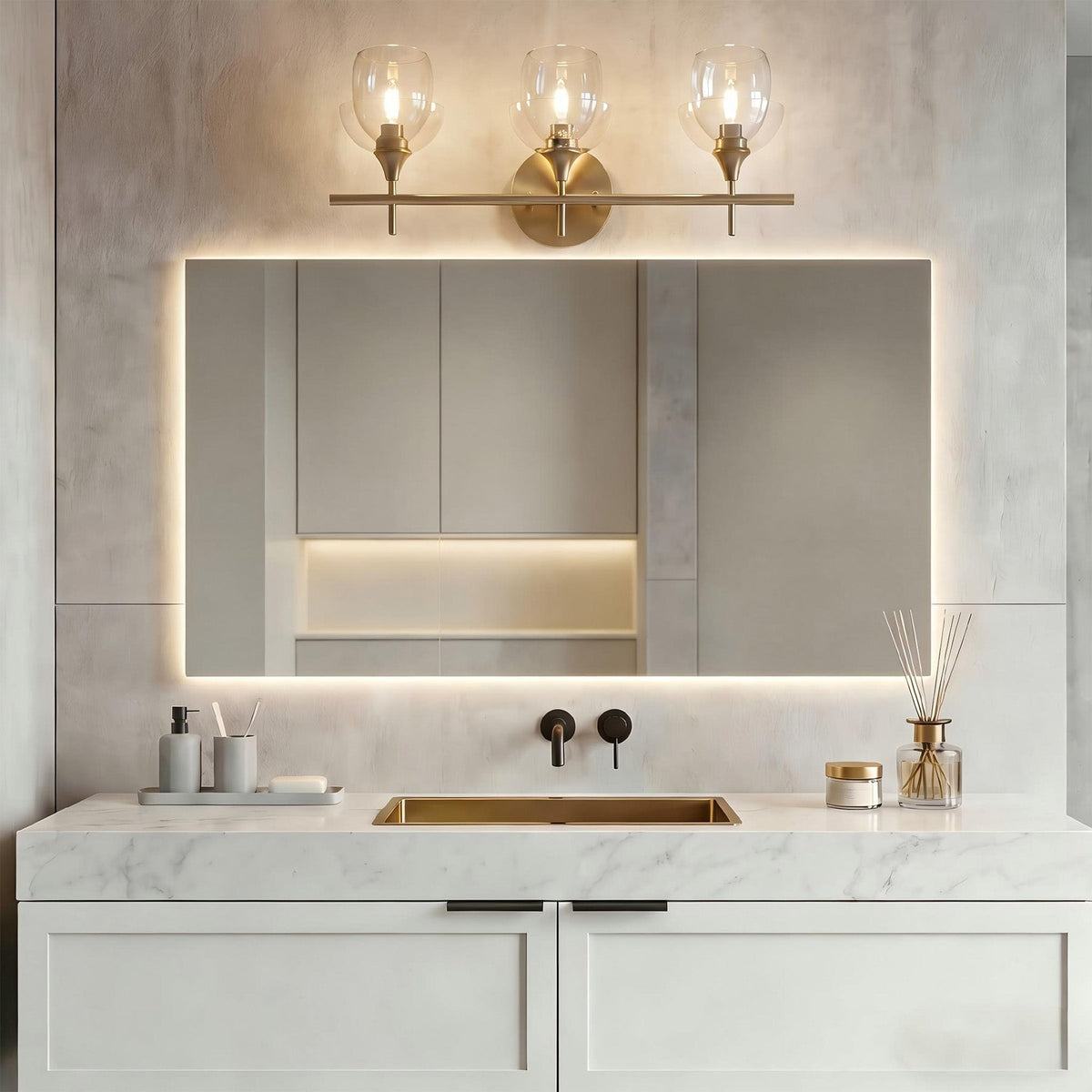 Gold bathroom vanity light with three clear glass shades mounted above a mirror
