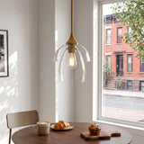 Gold pendant light with tiered clear glass shade hanging over a wooden table near a window