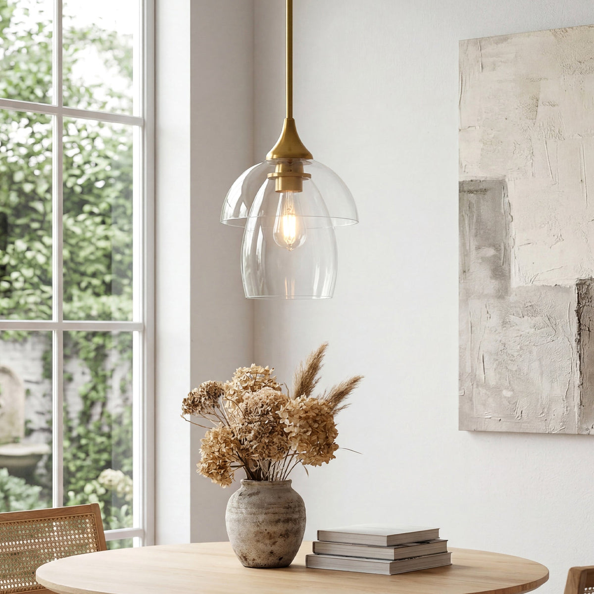 Gold pendant light with tiered clear glass shade, shown from side angle over wooden table near window