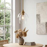 Gold pendant light with tiered clear glass shade, shown from side angle over wooden table near window