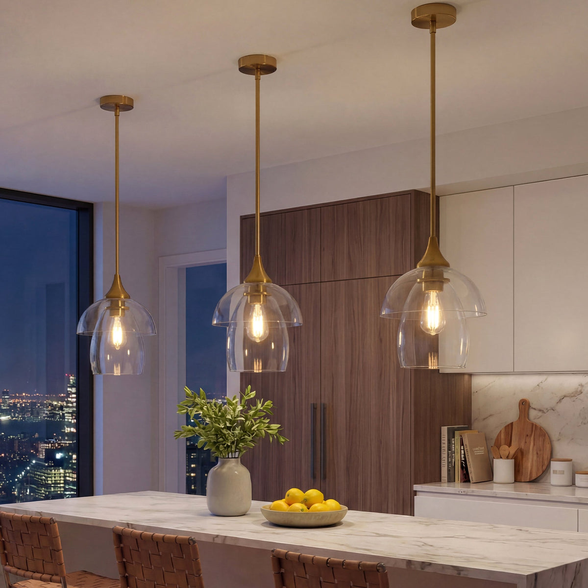 Three gold pendant lights with tiered clear glass shades hang over a kitchen island at night