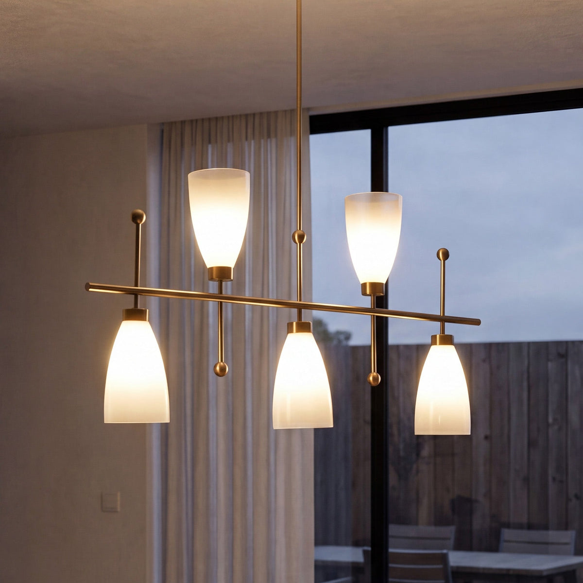 Five-light brushed brass chandelier with gradient frosted glass shades, hanging in a room with large window