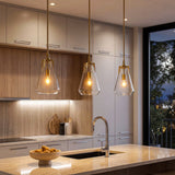 Three gold pendant lights with clear glass shades hang over a kitchen island