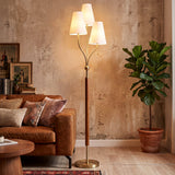 Gold floor lamp with three linen shades and rubberwood handle, shown in a living room setting