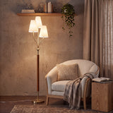 Gold floor lamp with three linen shades and rubberwood handle, angled in a cozy room setting