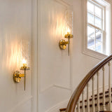 Two gold wall sconces with textured glass shades mounted on a white wall beside a staircase and window
