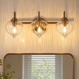 Three-light gold bathroom vanity light with pumpkin-shaped glass shades mounted above a mirror