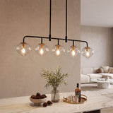 Five-light linear pendant with clear glass shades and black metal frame, hanging over a marble kitchen island