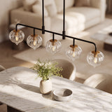 Five-light linear pendant with clear ribbed glass shades and black metal frame over marble dining table