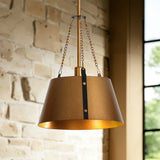 Gold drum pendant light with industrial metal shade, hanging from chains against brick wall